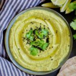 Green hummus on a plate with limes and cilantro.