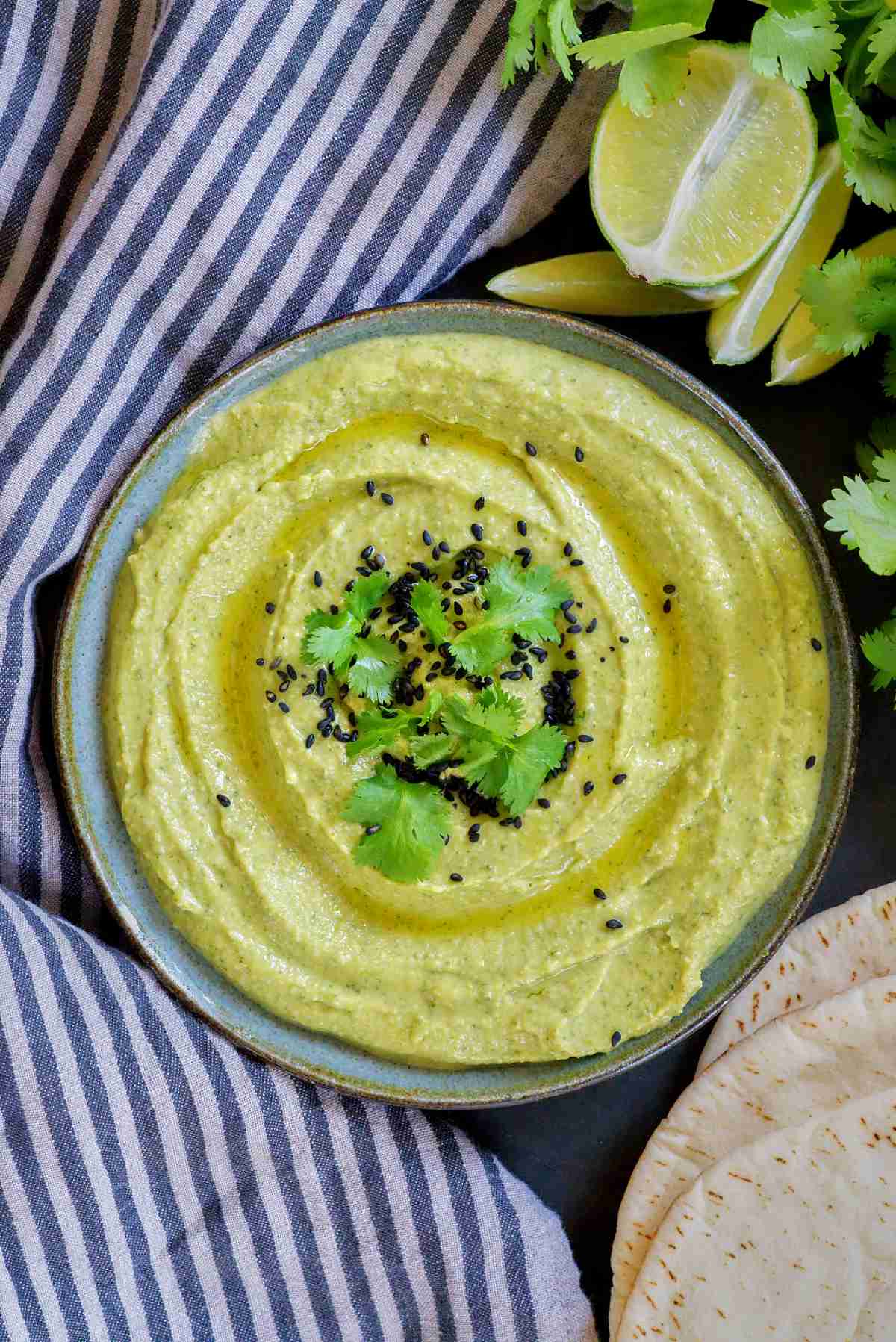 Green hummus on a plate with limes and cilantro.