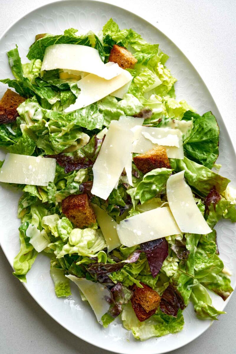 Caesar salad on a plate with croutons and large pieces of shaved parmesan.