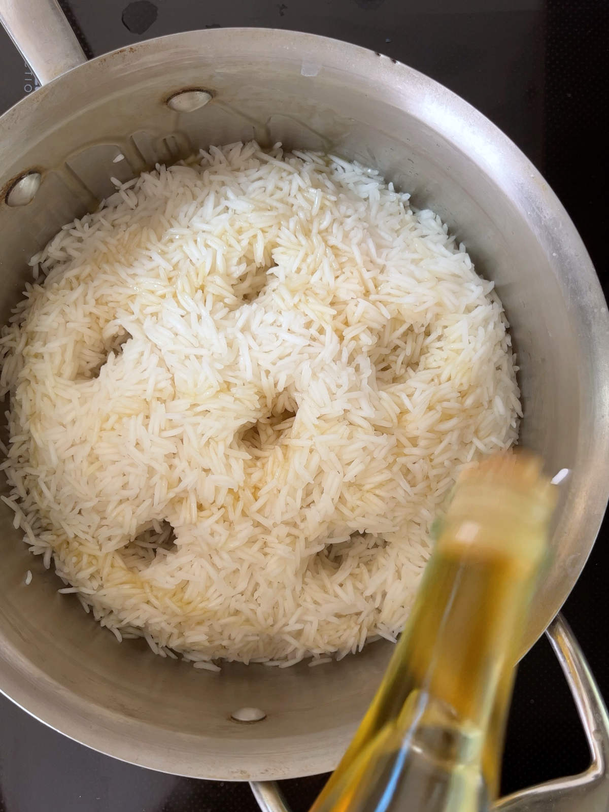 Pouring oil into a metal pot of rice with holes in the rice.
