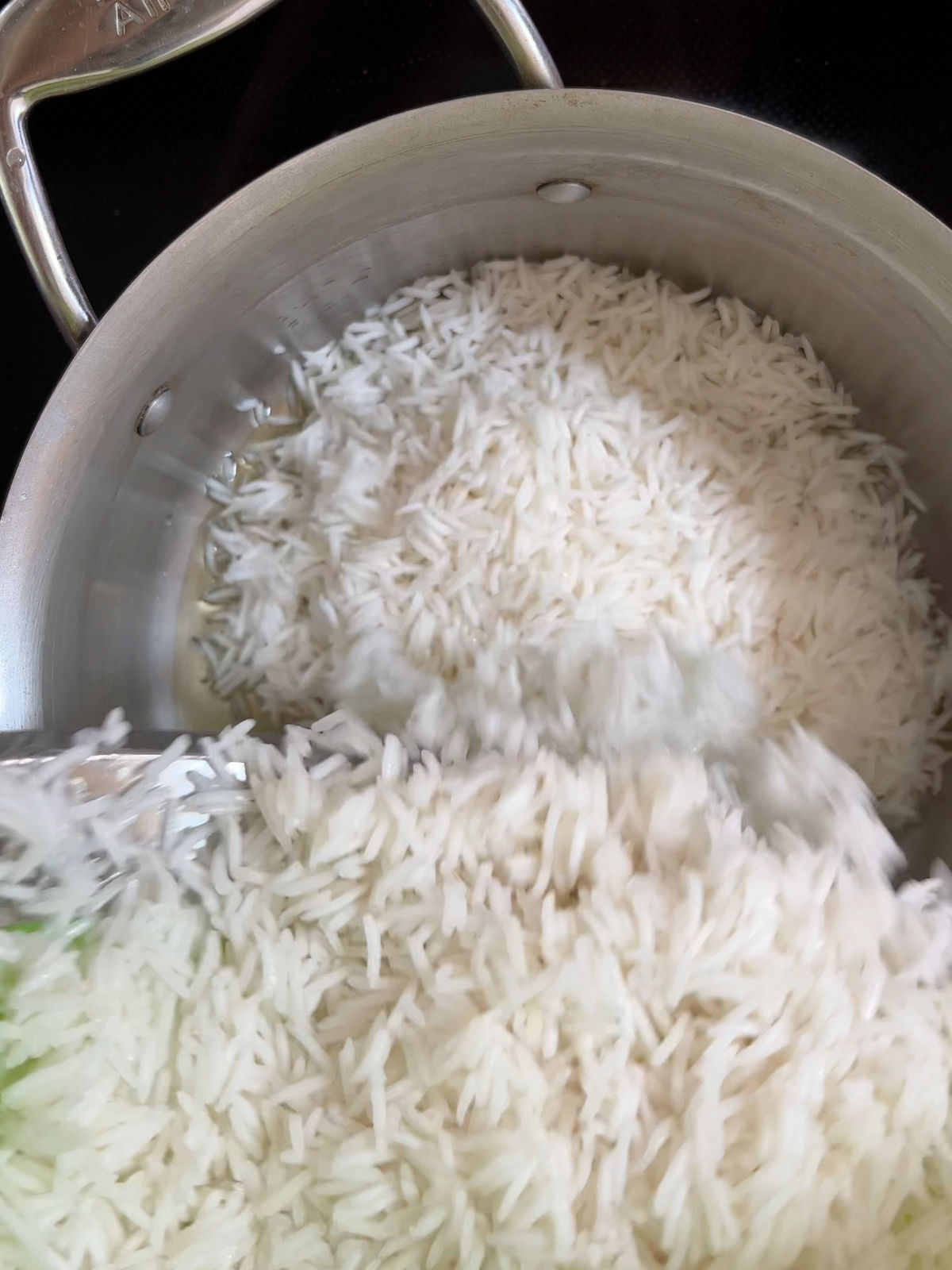 Pouring rice into a metal pot on a black stove.