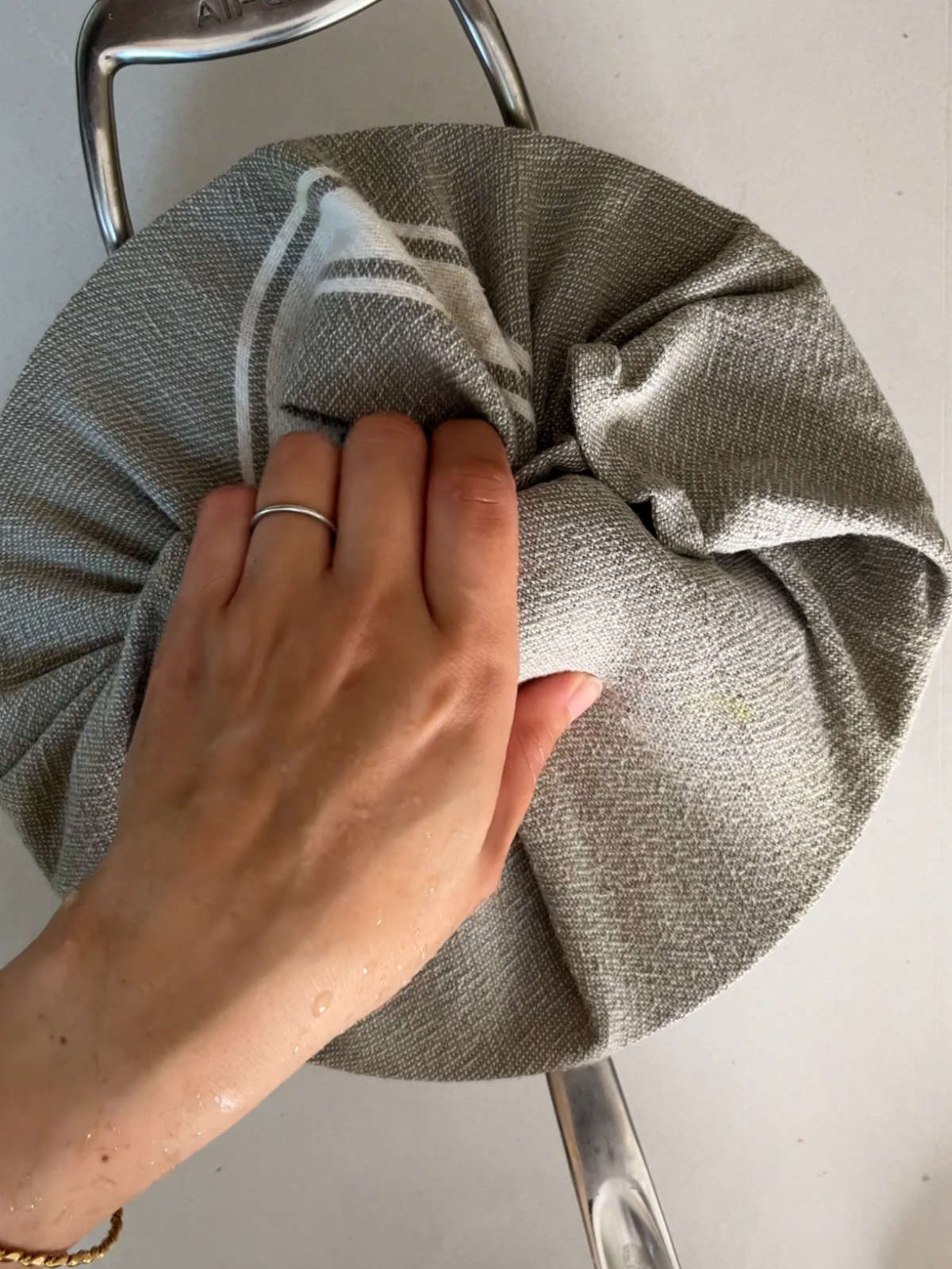 Hand holding the lid of a pot wrapped in a grey tea towel.