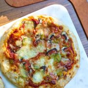 Pizza on a white table next to a pizza peel and edges of three other pizzas.