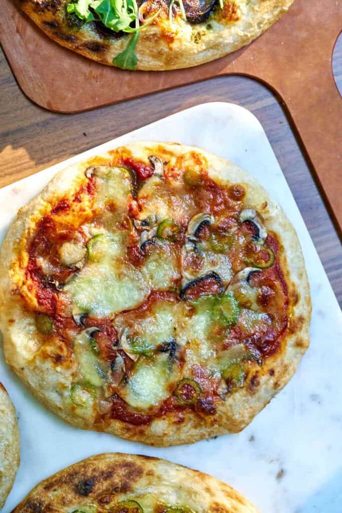 Pizza on a white table next to a pizza peel and edges of three other pizzas.