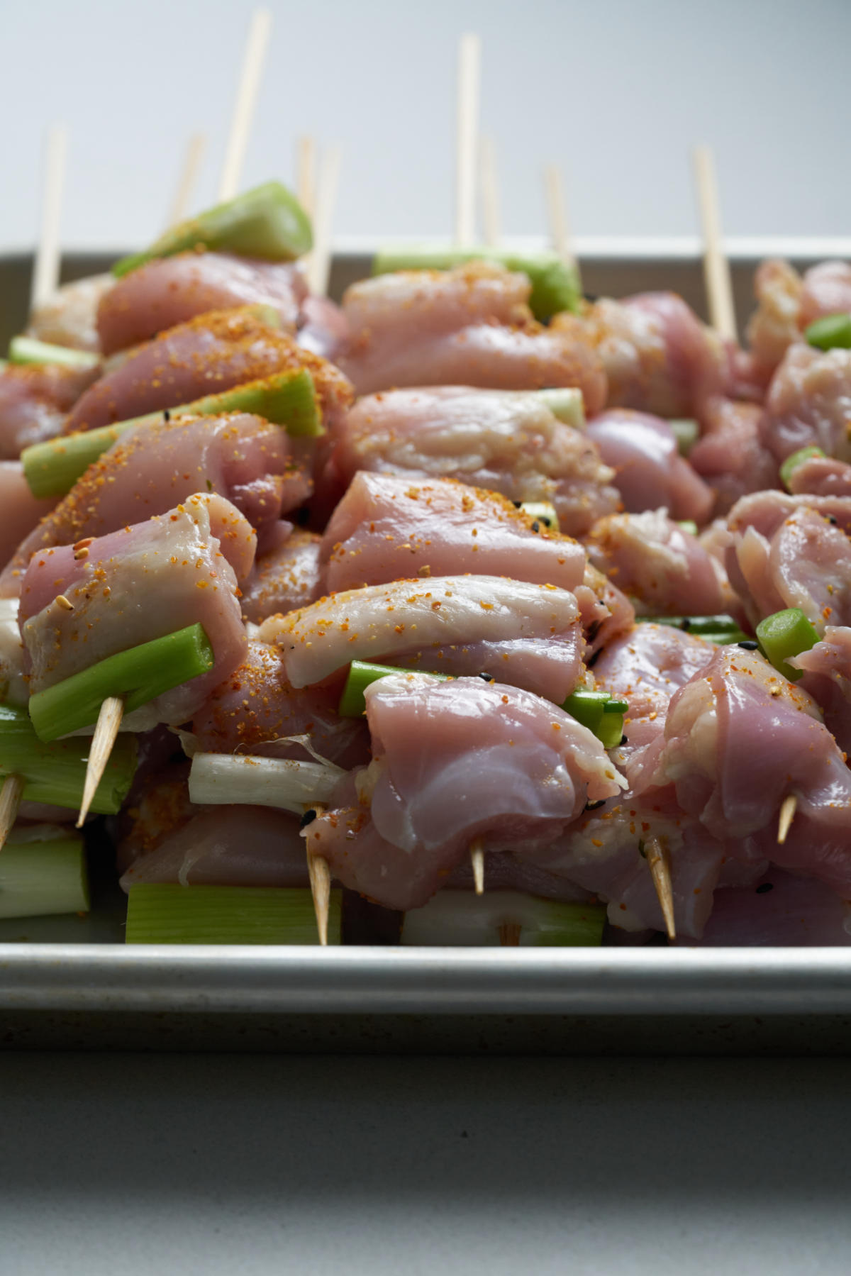 Raw chicken kabobs on skewers with scallions.