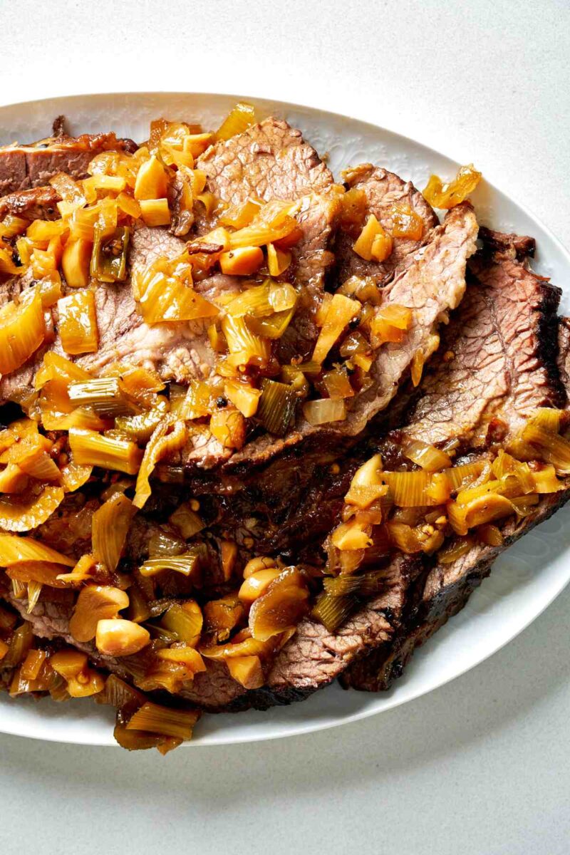 Sliced brisket on a serving plate with chopped vegetables.