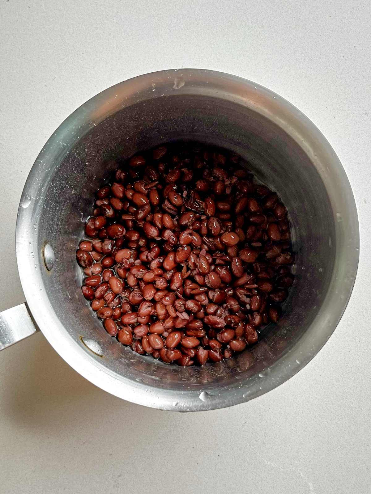 Black beans in a stainless steel pot on a countertop.