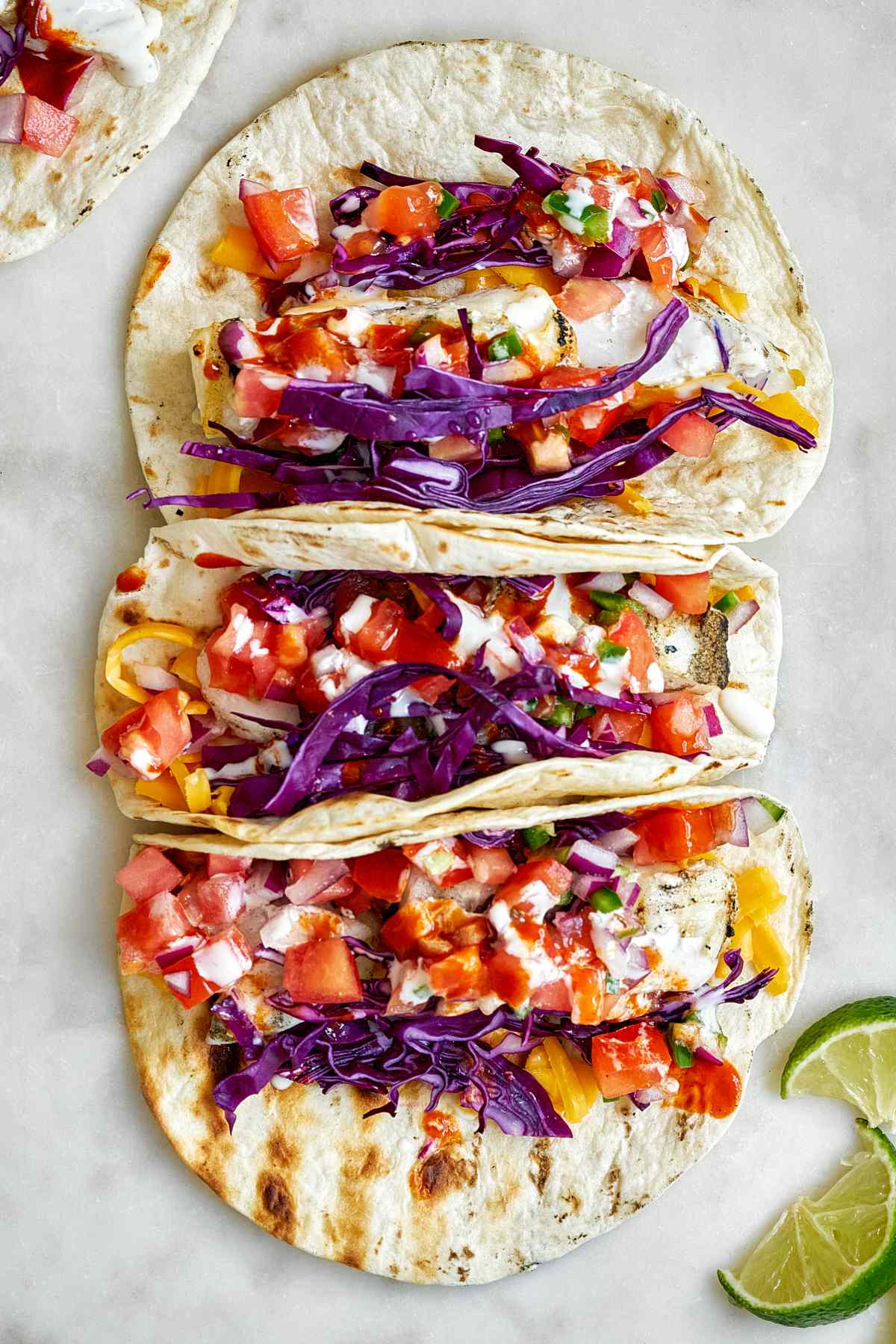 Four white fish tacos with pico de gallo, purple cabbage,  red onion topping.