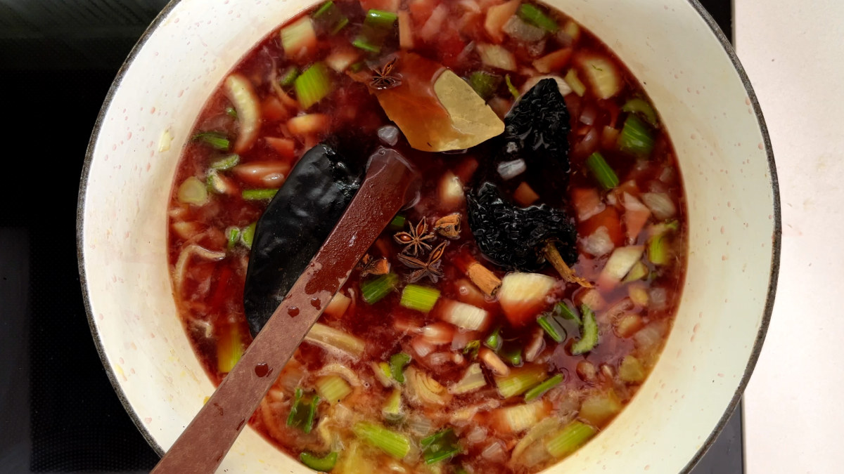 Chopped vegetables and dried chilis cooking in red wine in a white pot.