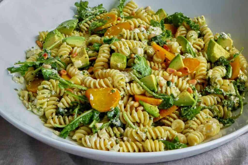 A full serving bowl of fussili pasta salad with greens, beets, and avocado. 