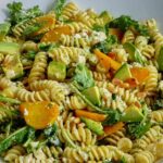 Close up of a serving bowl filled with pasta, avocado, cheese, and golden beets.