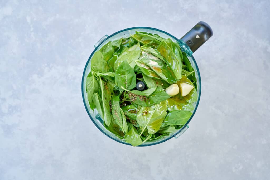 Ingredients to make pesto in a food processor bowl.