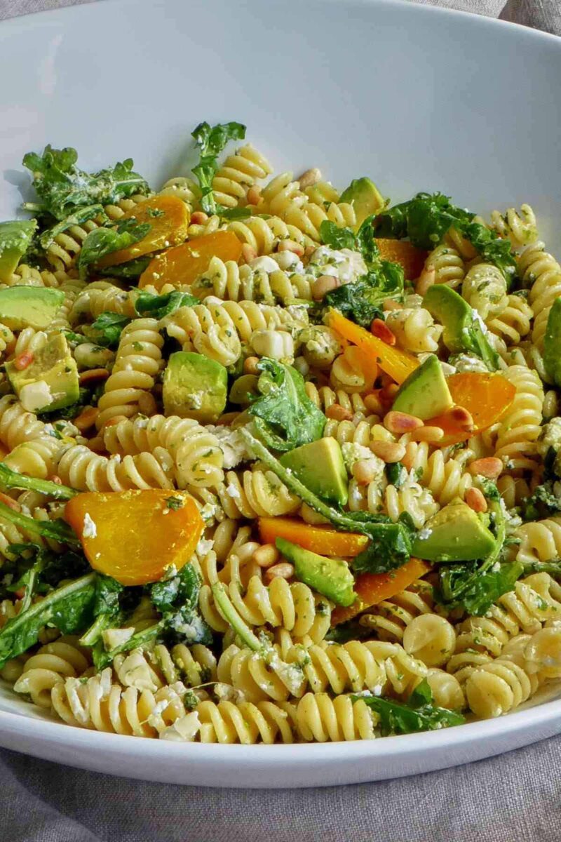 Close up of a serving bowl filled with pasta, avocado, cheese, and golden beets.