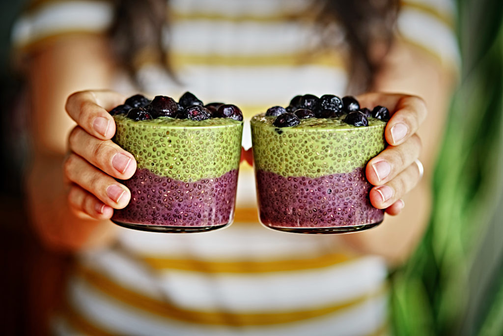 Girl holding layered chia pudding with green and purple chia pudding.