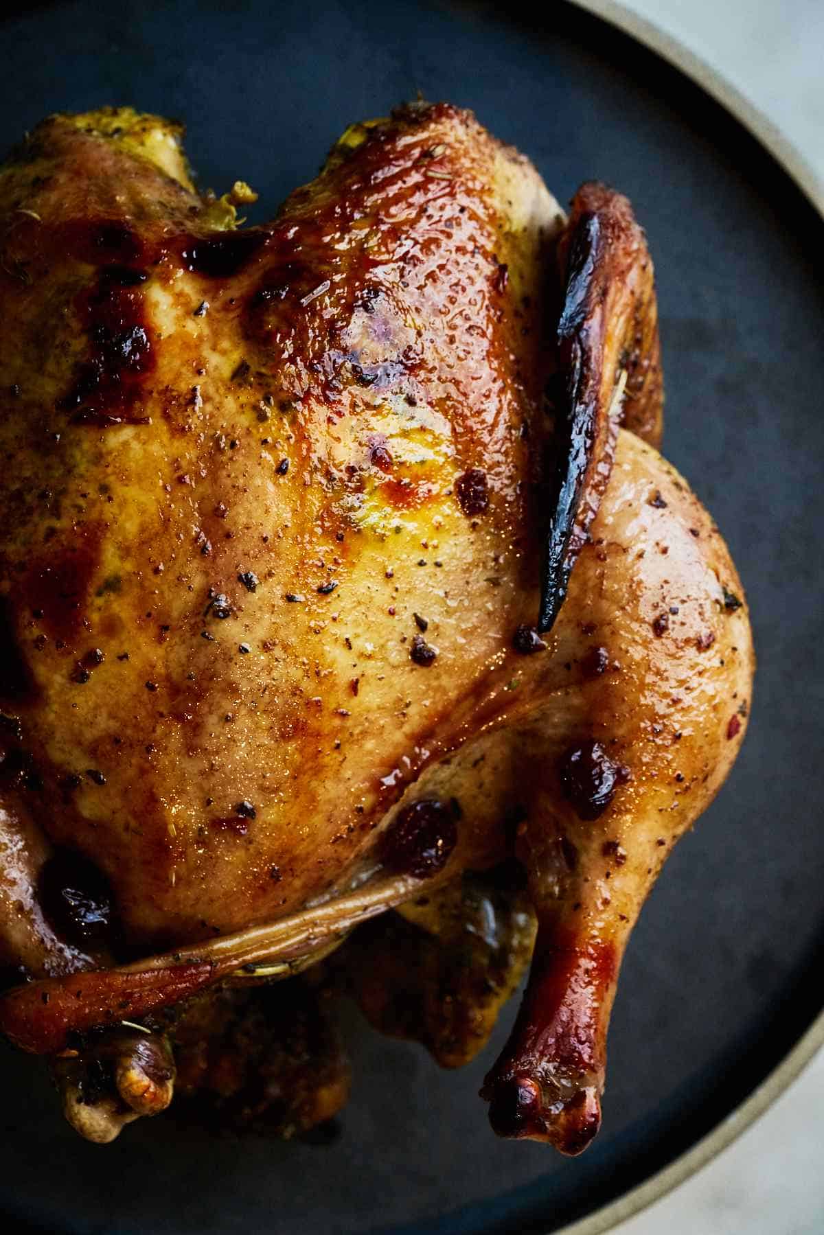 Roasted whole chicken on a black plate.