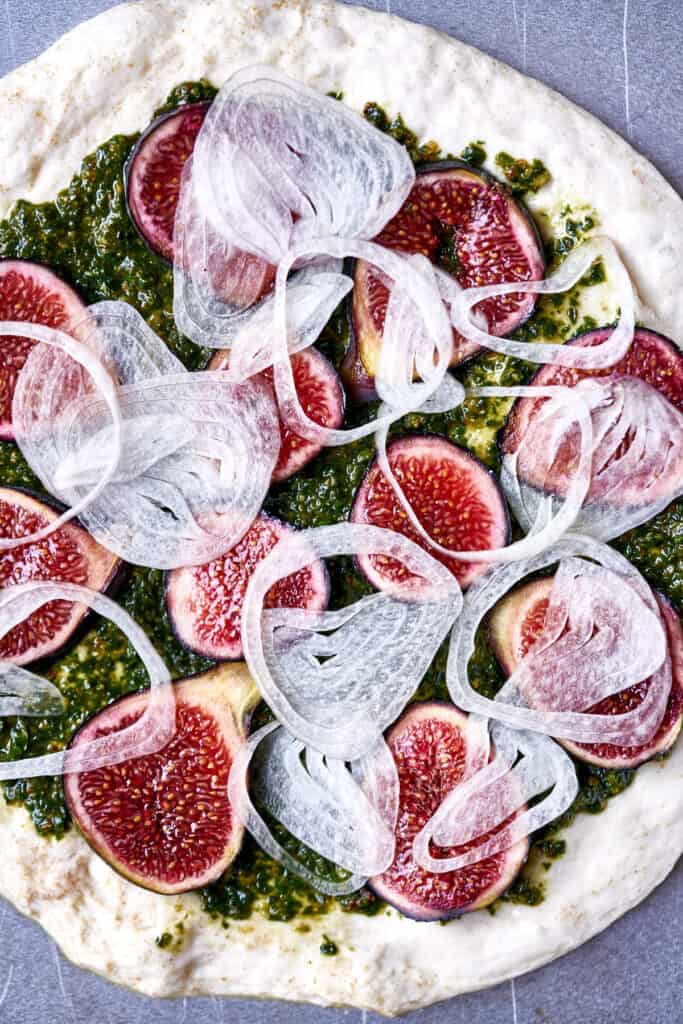 Top view of pizza dough covered in pesto, figs, and onion.