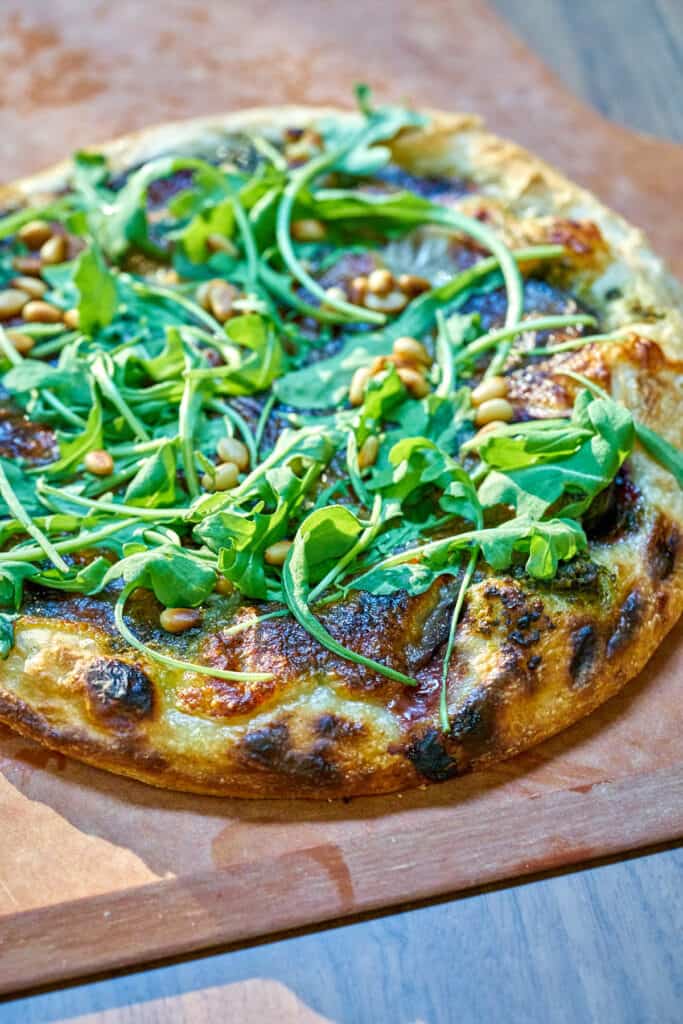 Pizza on a pizza peel with fresh arugula.