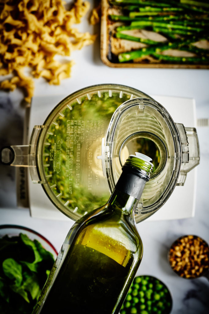 Pouring olive oil into a food processor.