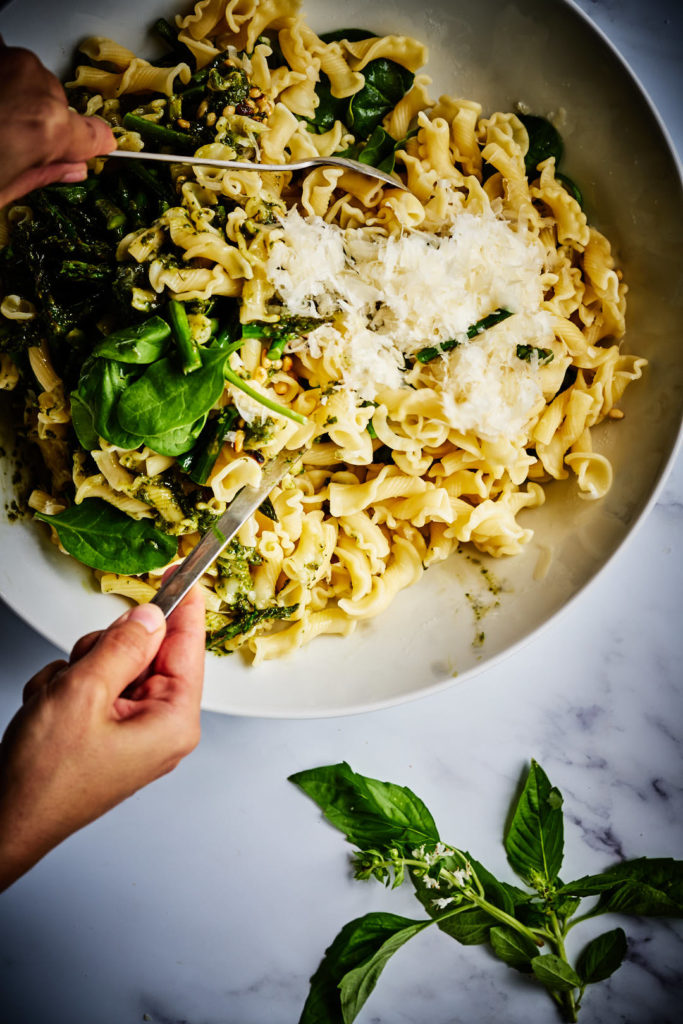 Mixing green pasta salad in a serving bowl.