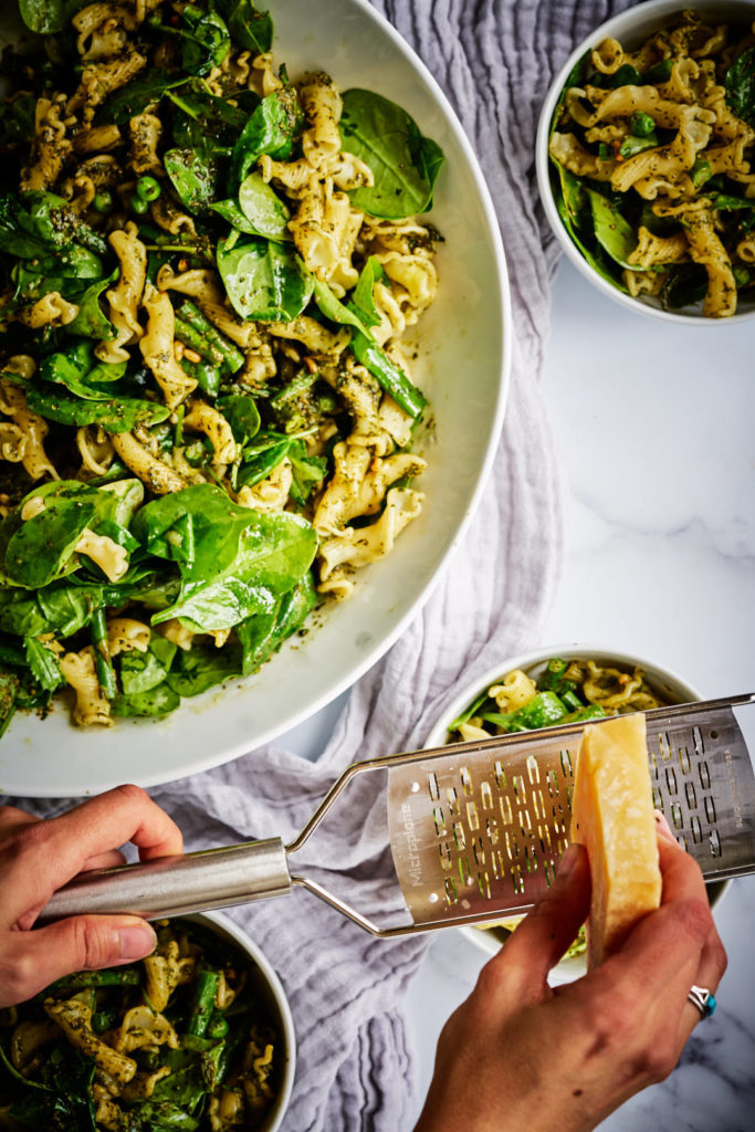 Shaving parmesan cheese over green pasta salad.