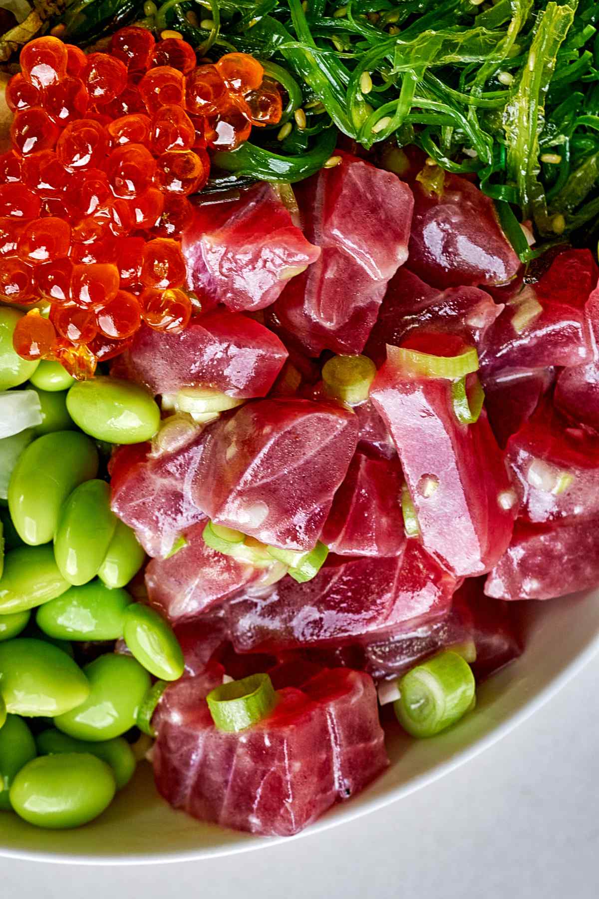 Tuna tartare in a bowl next to green vegetables and roe.