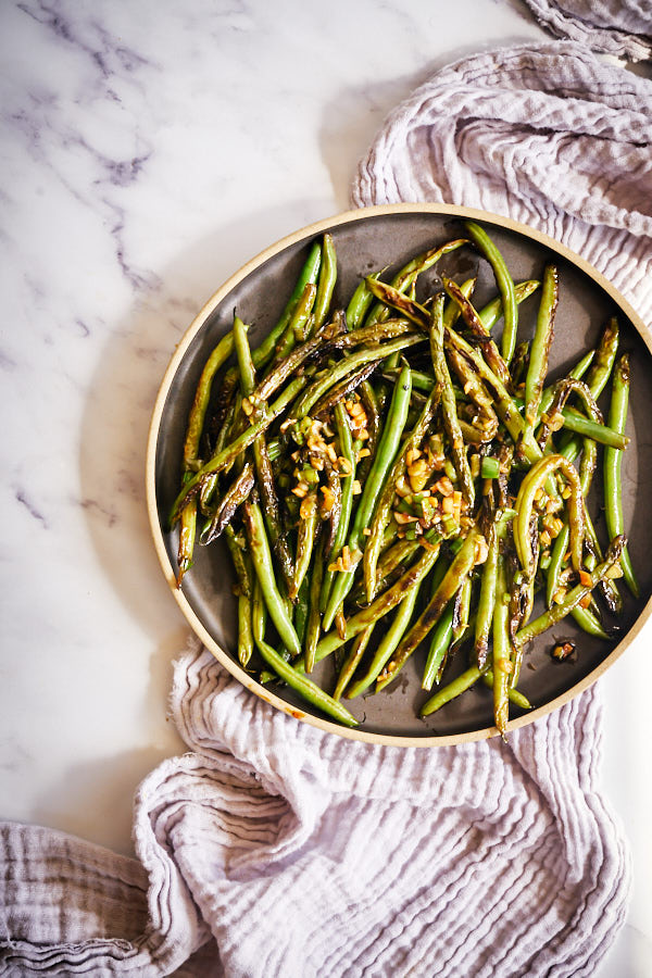 Overhead shot of cooked green beans in a round black plate.