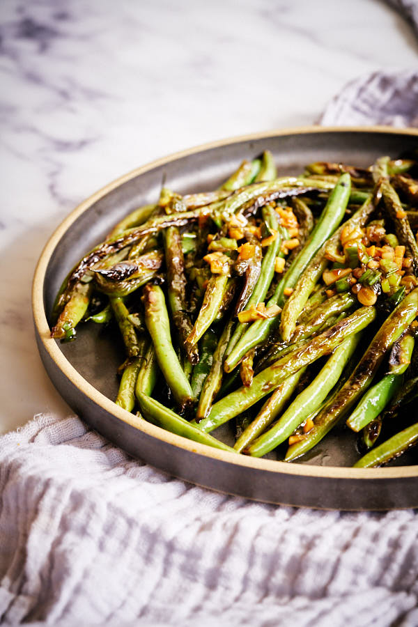 Cooked green beans on a round black plate.