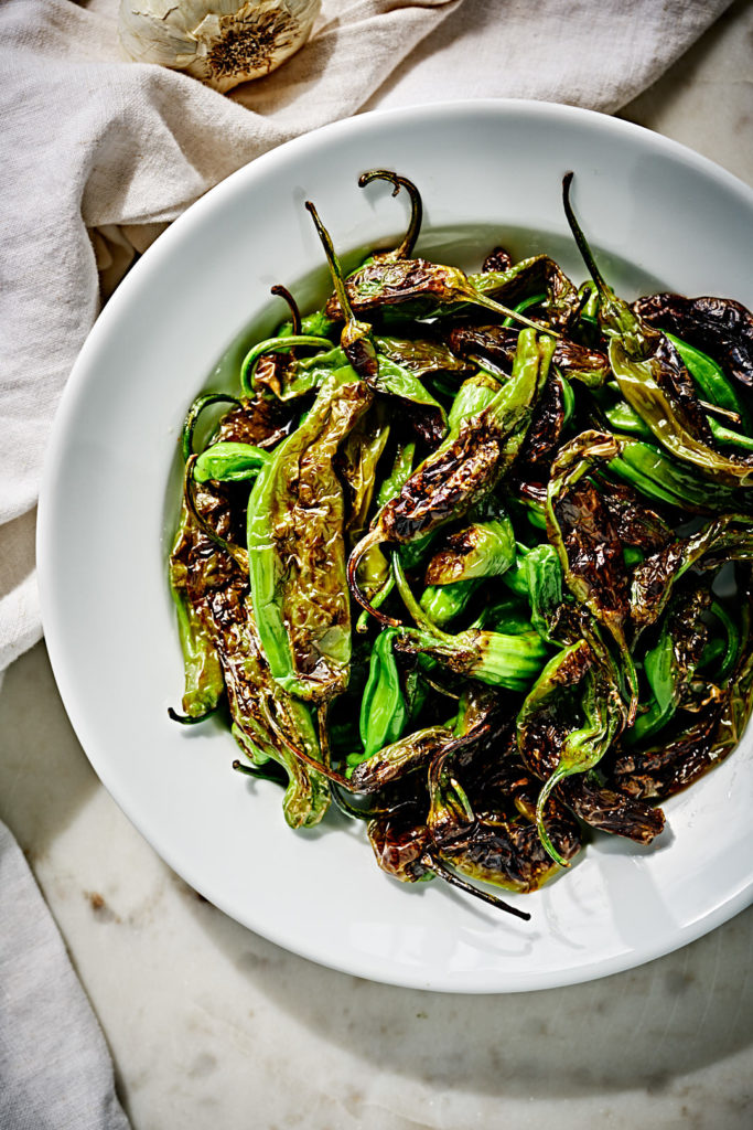 Blistered shishito peppers in a white plate.