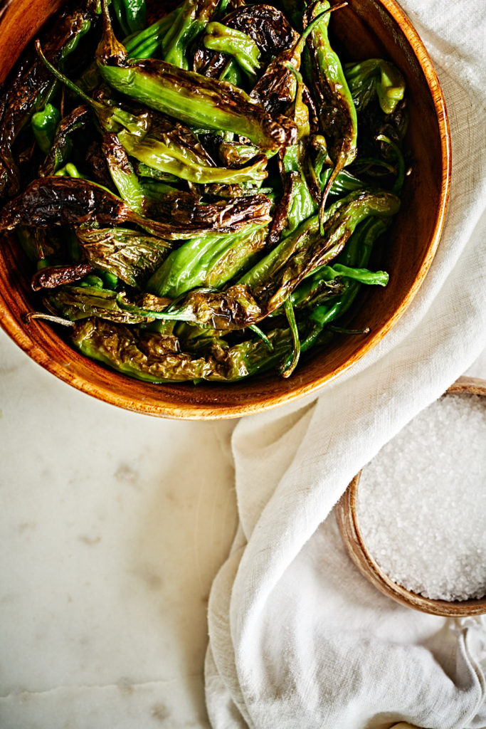 Shishito peppers in a wood bowl with salt.