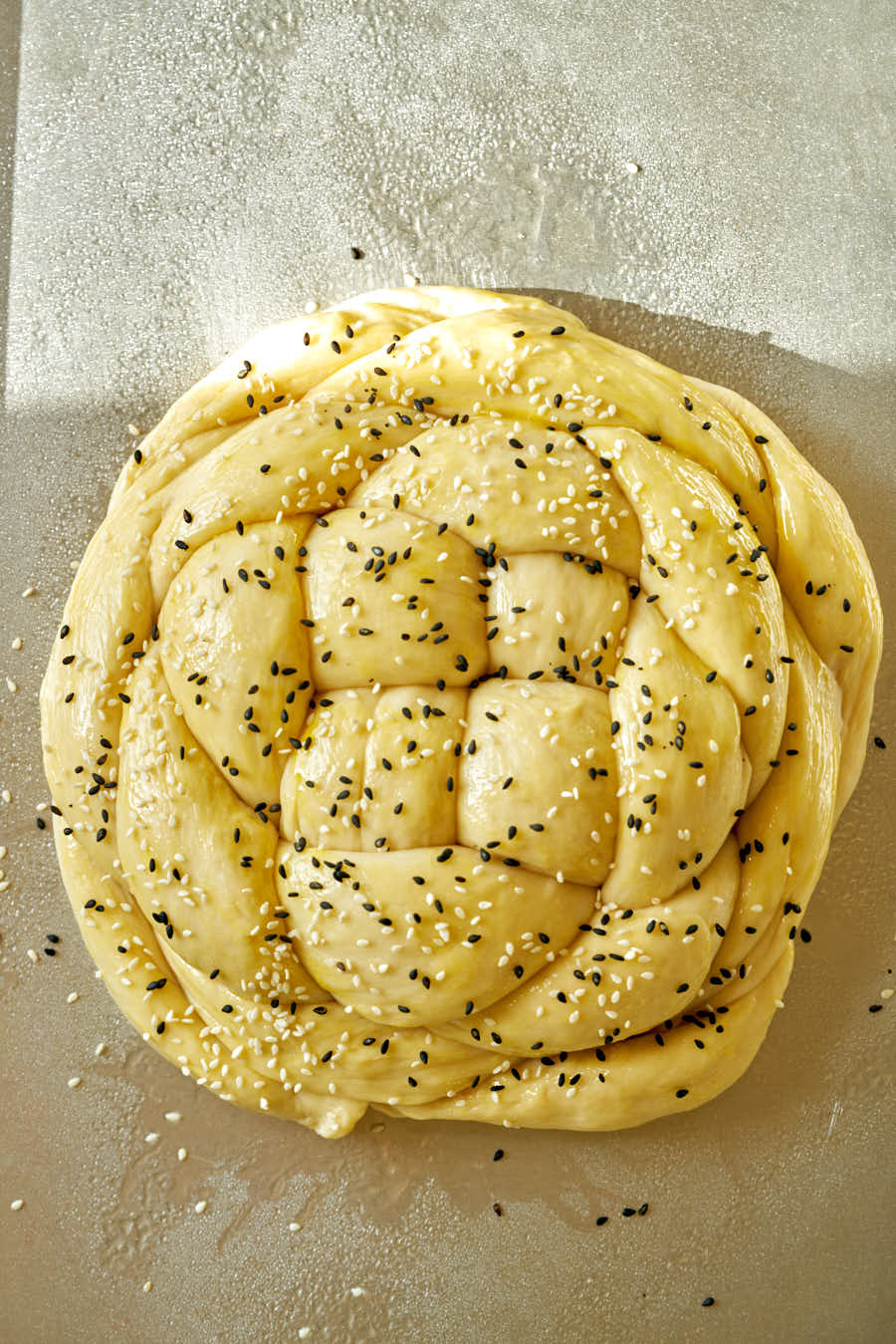 Raw round challah sprinkled with sesame seeds.