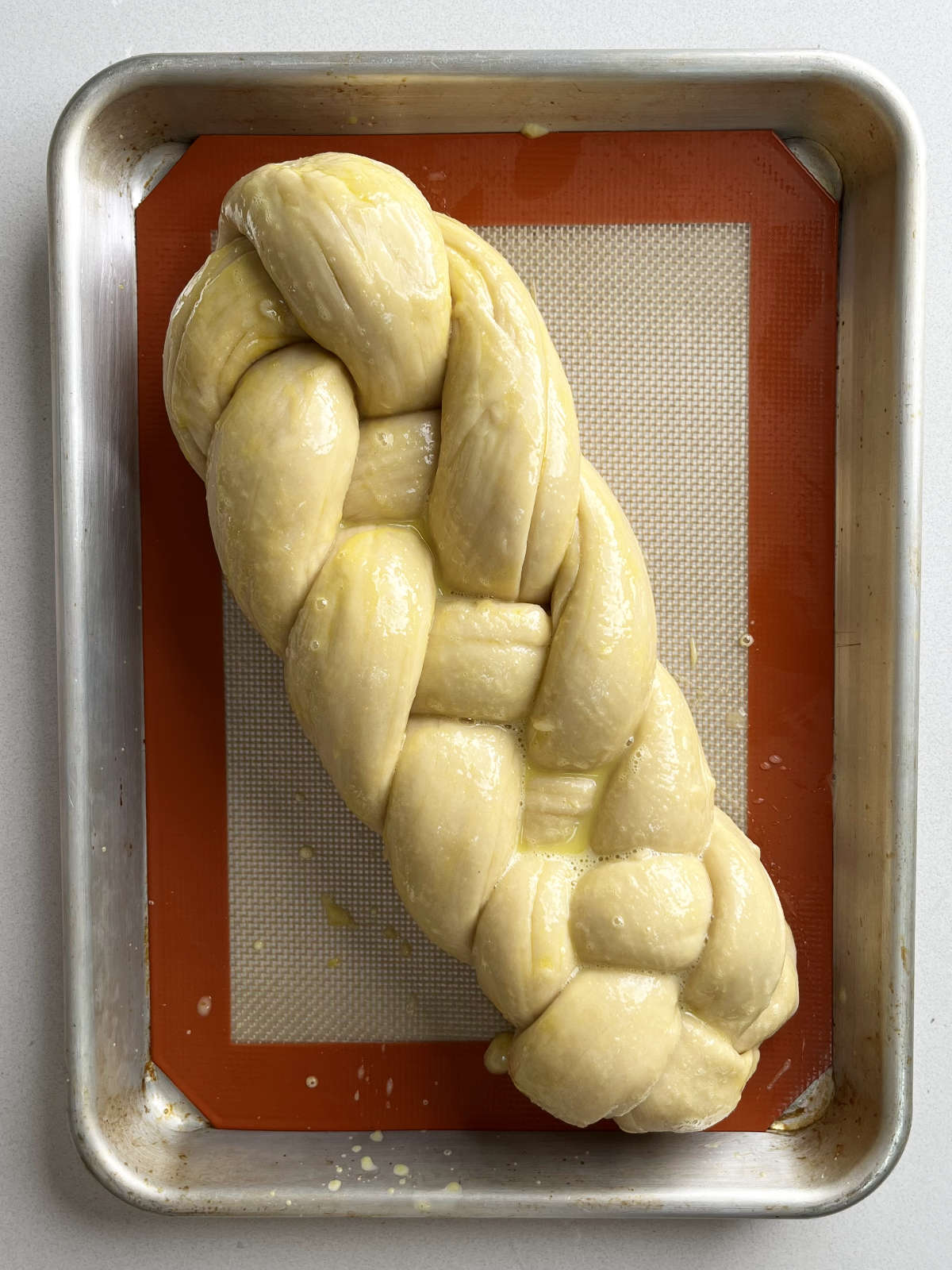 Four strand braid of a raw challah on a baking sheet lined with a silicone baking mat.