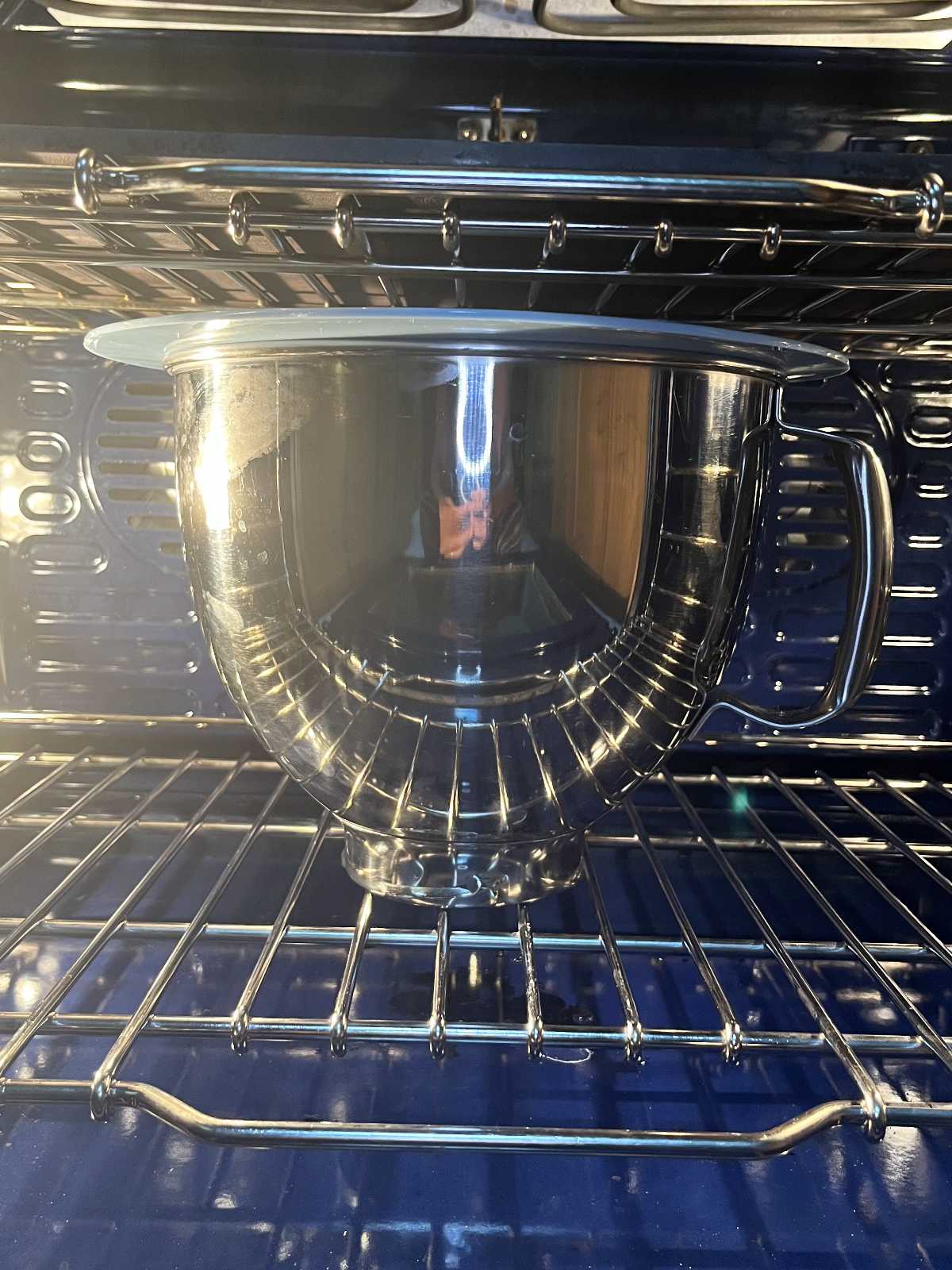 Stand mixer bowl in an oven with a blue silicone lid.