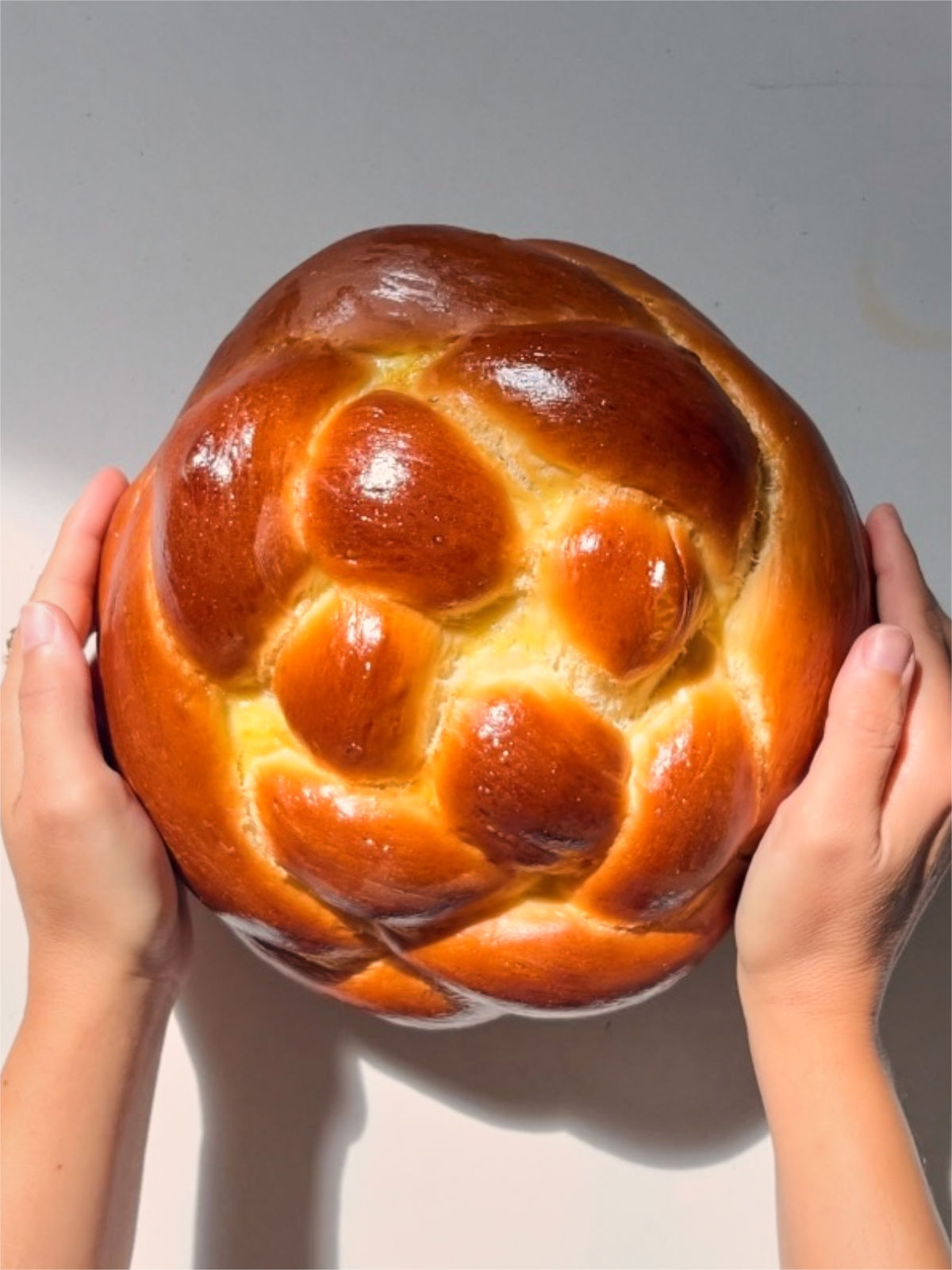 Round challah held in two hands on a countertop.