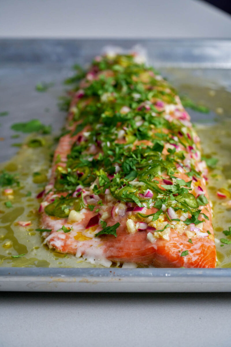 Front view of cooked salmon on a baking dish with herbs.