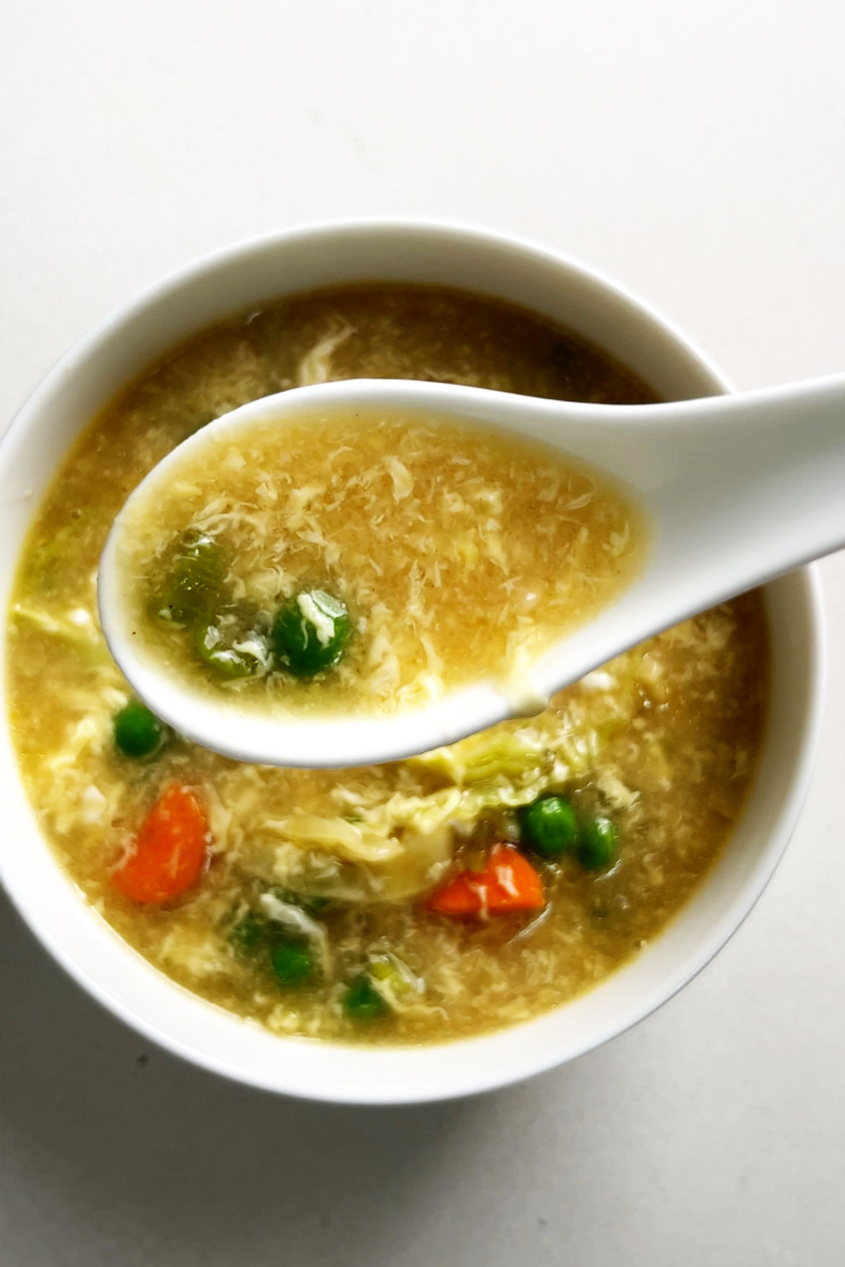 Egg drop soup on a spoon over a bowl of soup.