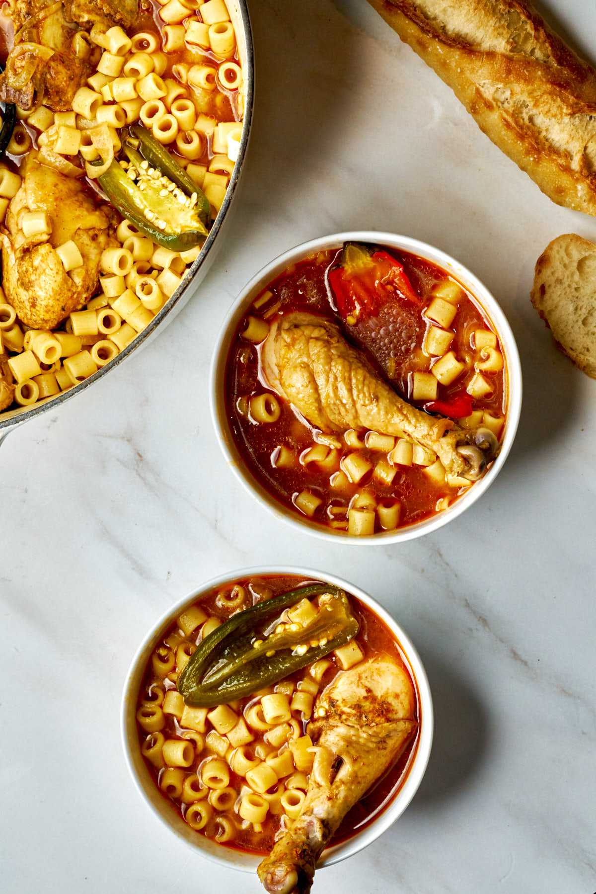 Two bowls of noodle soup with chicken legs.