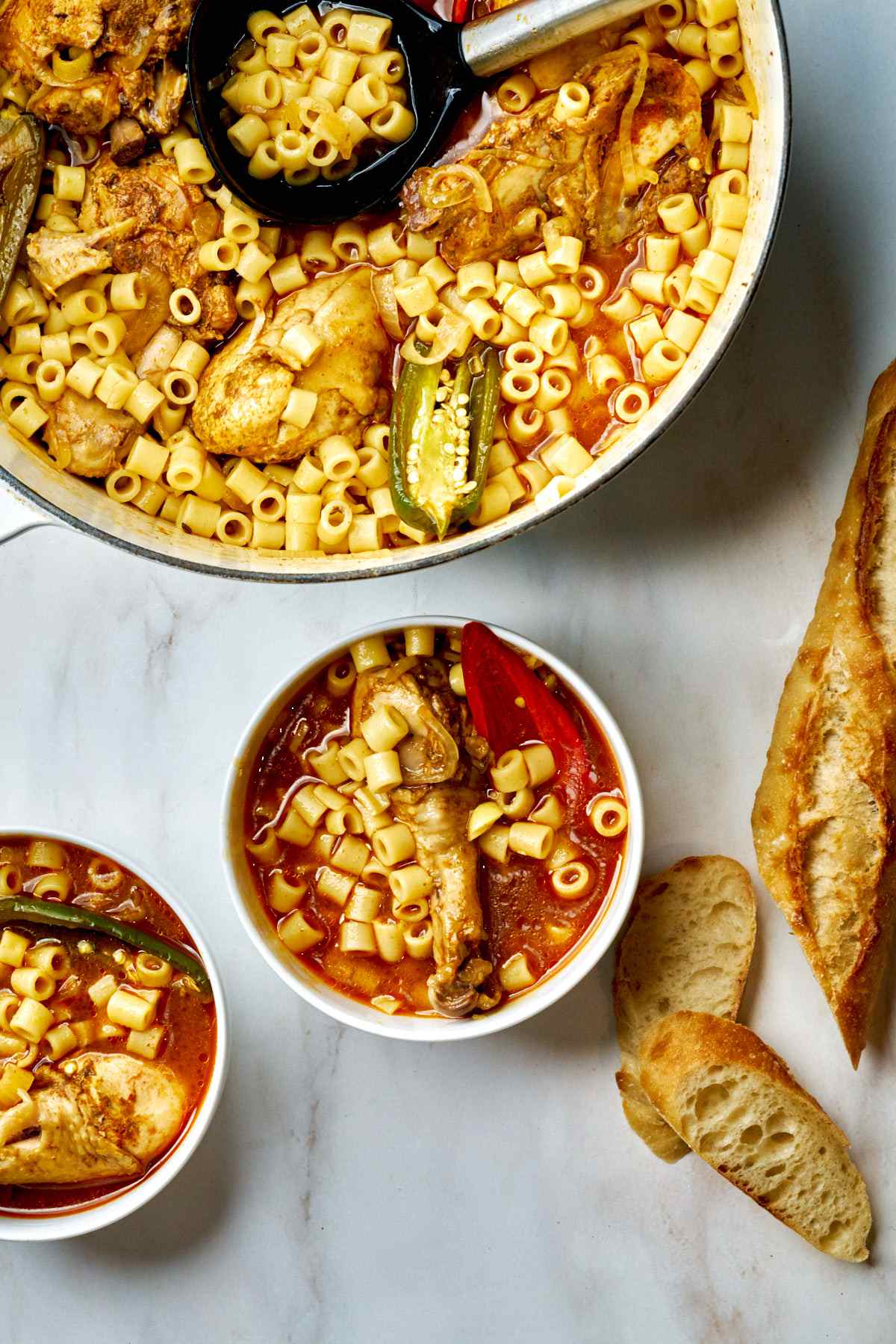 Bowl of noodle soup next to a pot of soup and bread.