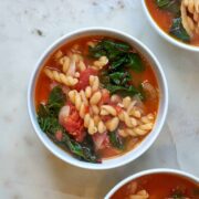 Three bowls of Bowl of red soup with noodles and greens.
