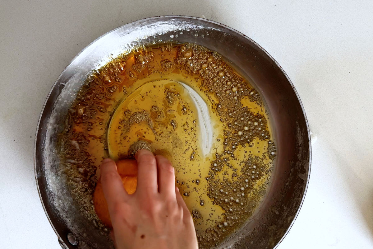 Hand swirling a doughnut in caramel.