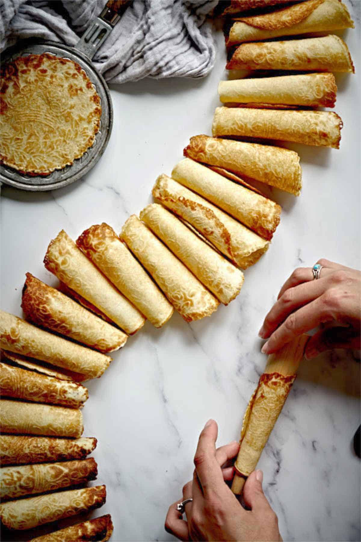 Rolling krumkake on wood cone on marble counter.