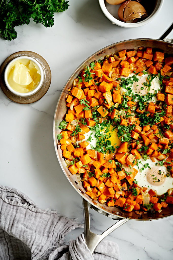 Sweet potato hash with eggs in a large silver pan on a marble backdrop.