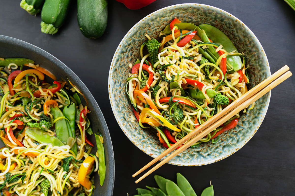 Noodles stir fry in a bowl with chop sticks.