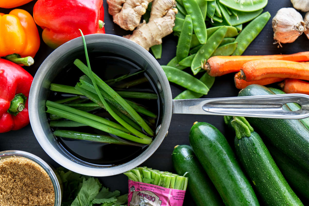 Scallions and sauce in a saucepan surrounded by vegetables.