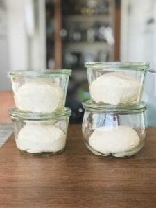 Four glass jars on a wood table with dough in them.