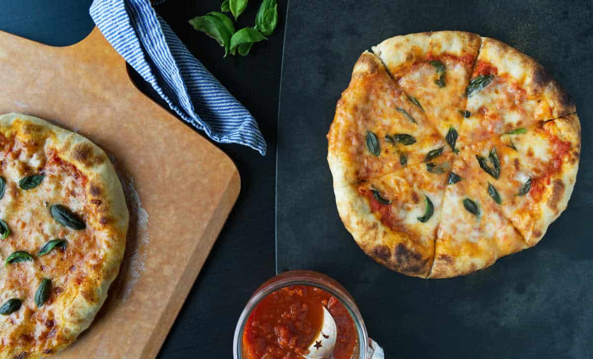 Two pizzas with basil, one on a black cutting board and the other on a pizza peel.