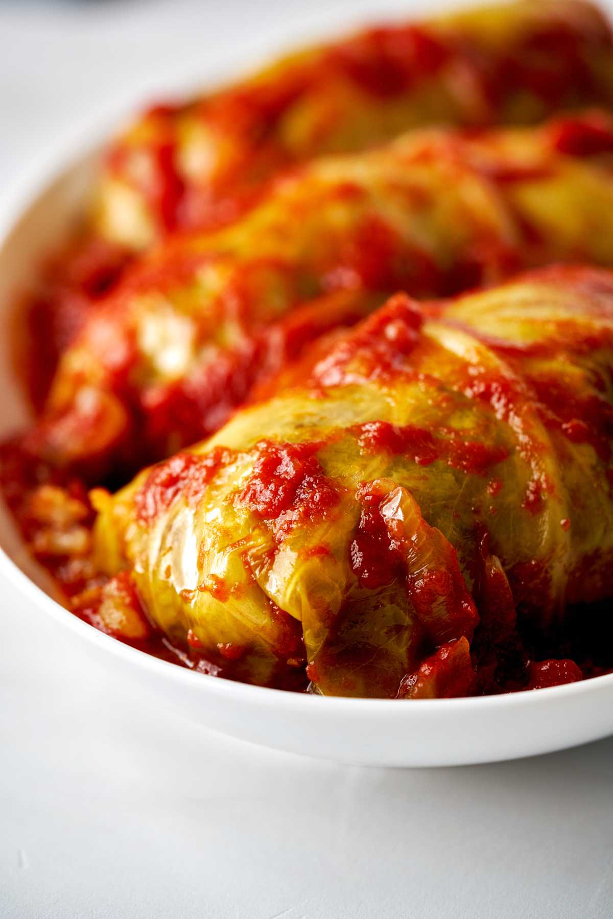 Cabbage rolls on a white plate covered in tomato sauce.