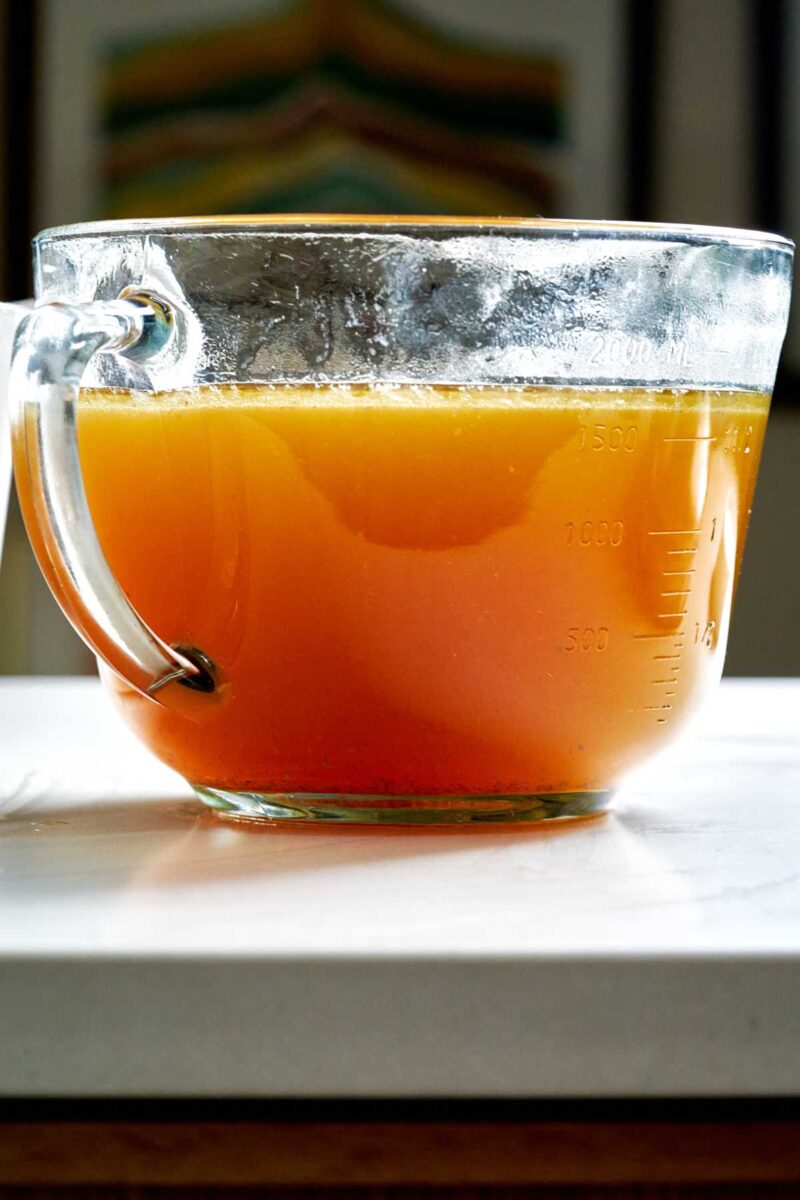 Large glass liquid measuring bowl filled with chicken stock.