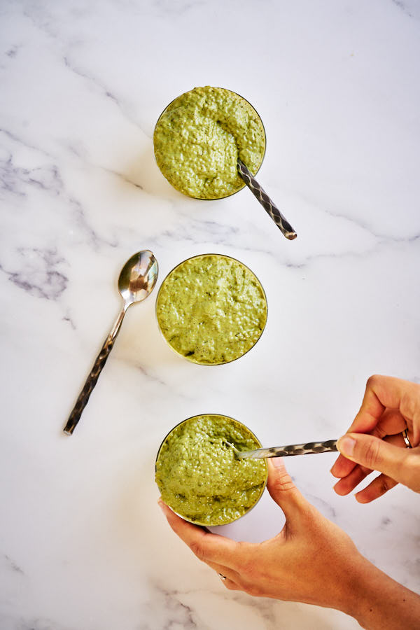 Three cups of matcha chia pudding with three metal spoons on a white marble counter.