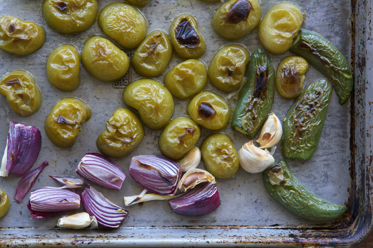 Charred tomatillos and onions on a baking sheet.