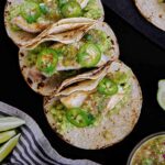 Three tacos topped with green salsa.